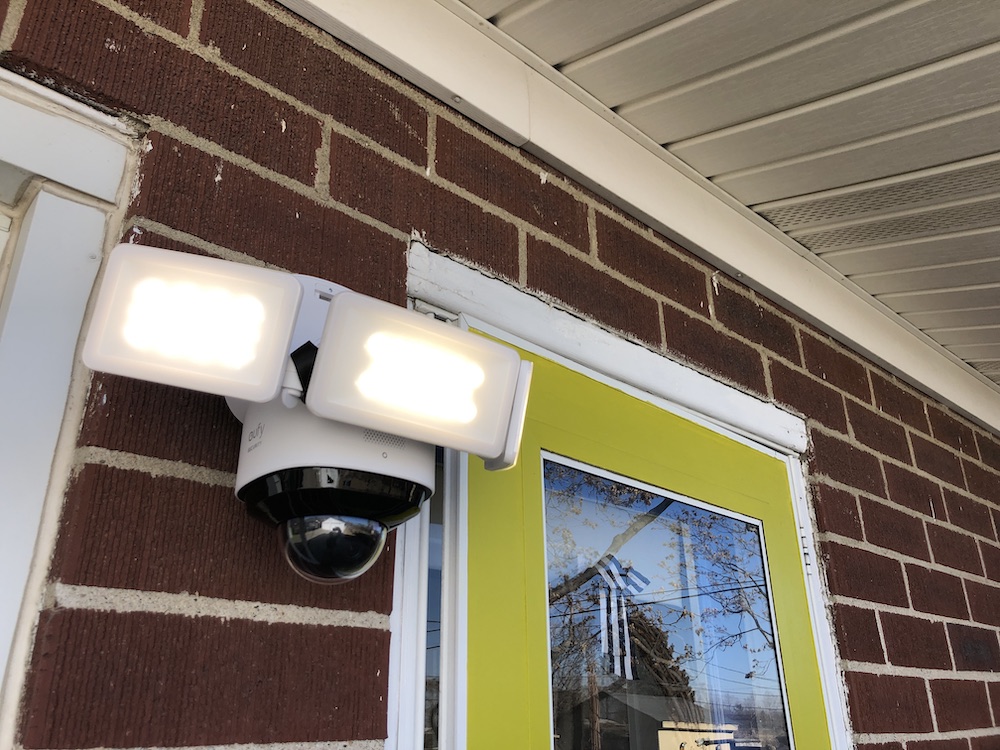 Eufy 360 Floodlight installed on a home with a brick wall and yellow door.