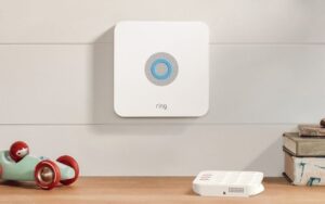 A wall-mounted Ring security base station with an illuminated indicator, part of a home monitoring system.