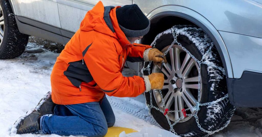 Man in orange parka putting snow chains on a tire.