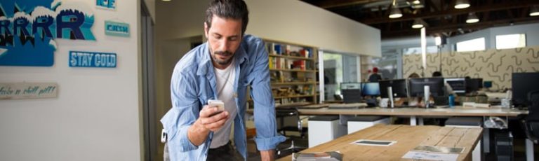 A man holding an iphone checking his Vivint app to see his home security system status.