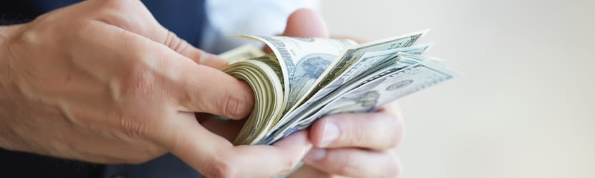 A man unfurling $100 bills in his hand.