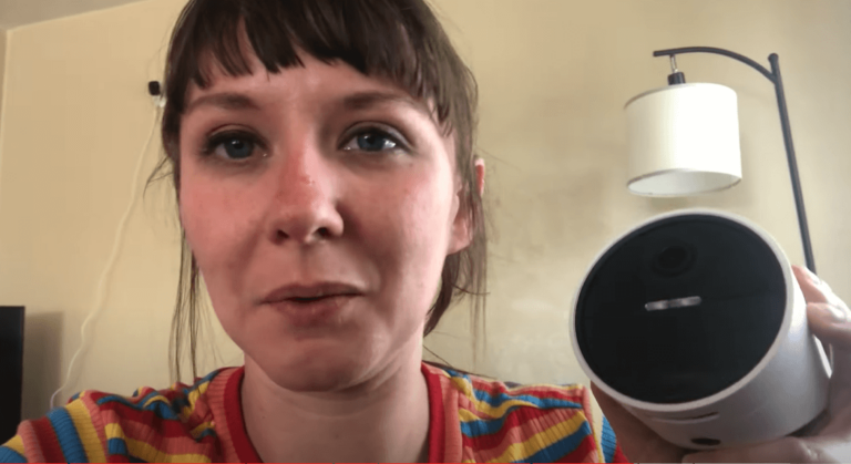A user holding a SimpliSafe outdoor security camera while testing its features in a home setting.