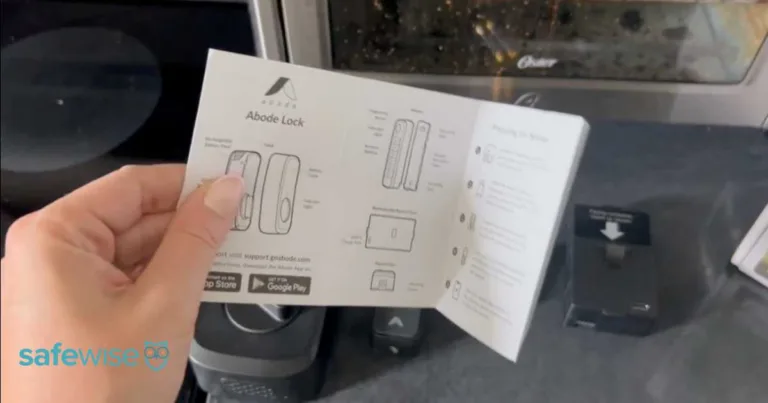 Hand holding the installation instruction booklet for the Abode Smart Lock.