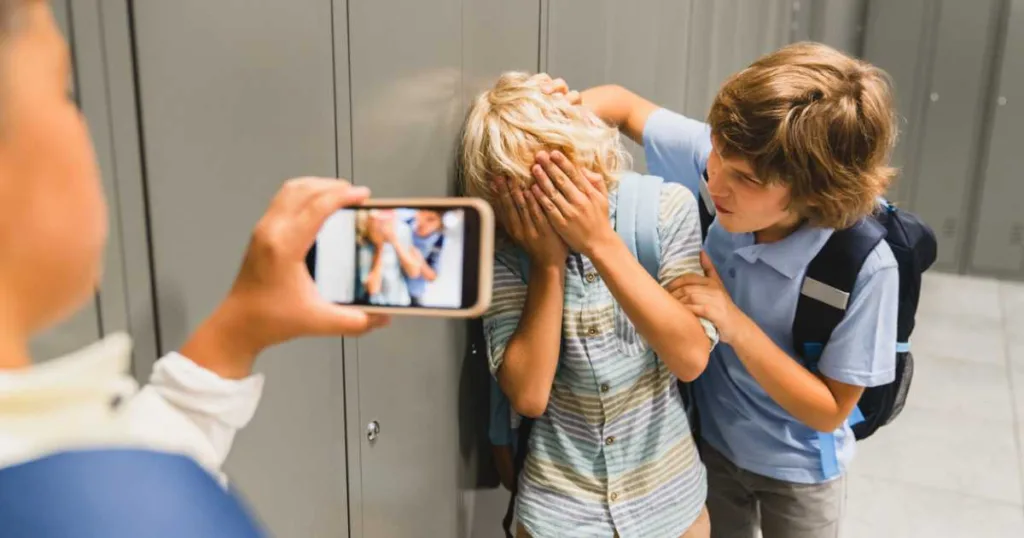 Boys filming on the phone bullying their classmate in school hall.