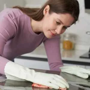A woman cleans an induction stovetop with gloves on to protect her hands. Get the price on Amazon.