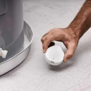 A homeowner places the Moen Flo water leak sensor by the hot water heater. Get more details and pricing on Amazon.
