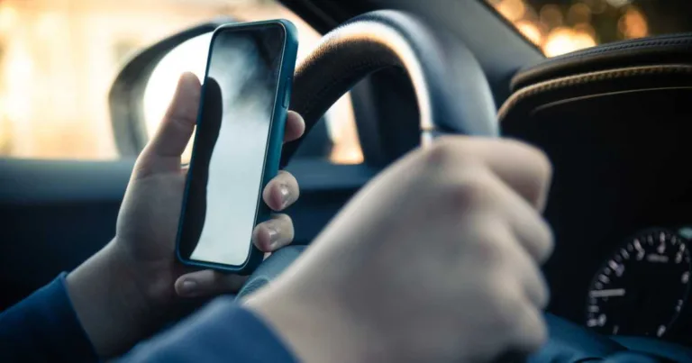Teen driver with one hand on the wheel and a phone in the other hand.