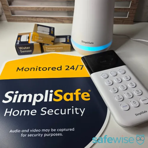 A SimpliSafe yard sign displayed with the alarm system's base station, keypad, and an entry sensor.